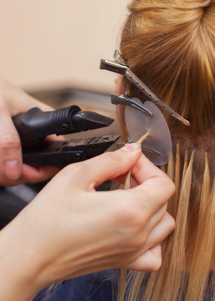 The hairdresser does hair extensions to a young girl, a blonde i